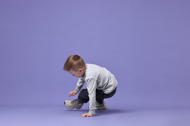 Photo of Happy little boy dancing on violet background. Space for text