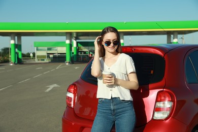 Photo of Beautiful young woman with coffee near car at gas station
