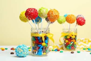 Photo of Glass jars with tasty cake pops and dragee on table against yellow background