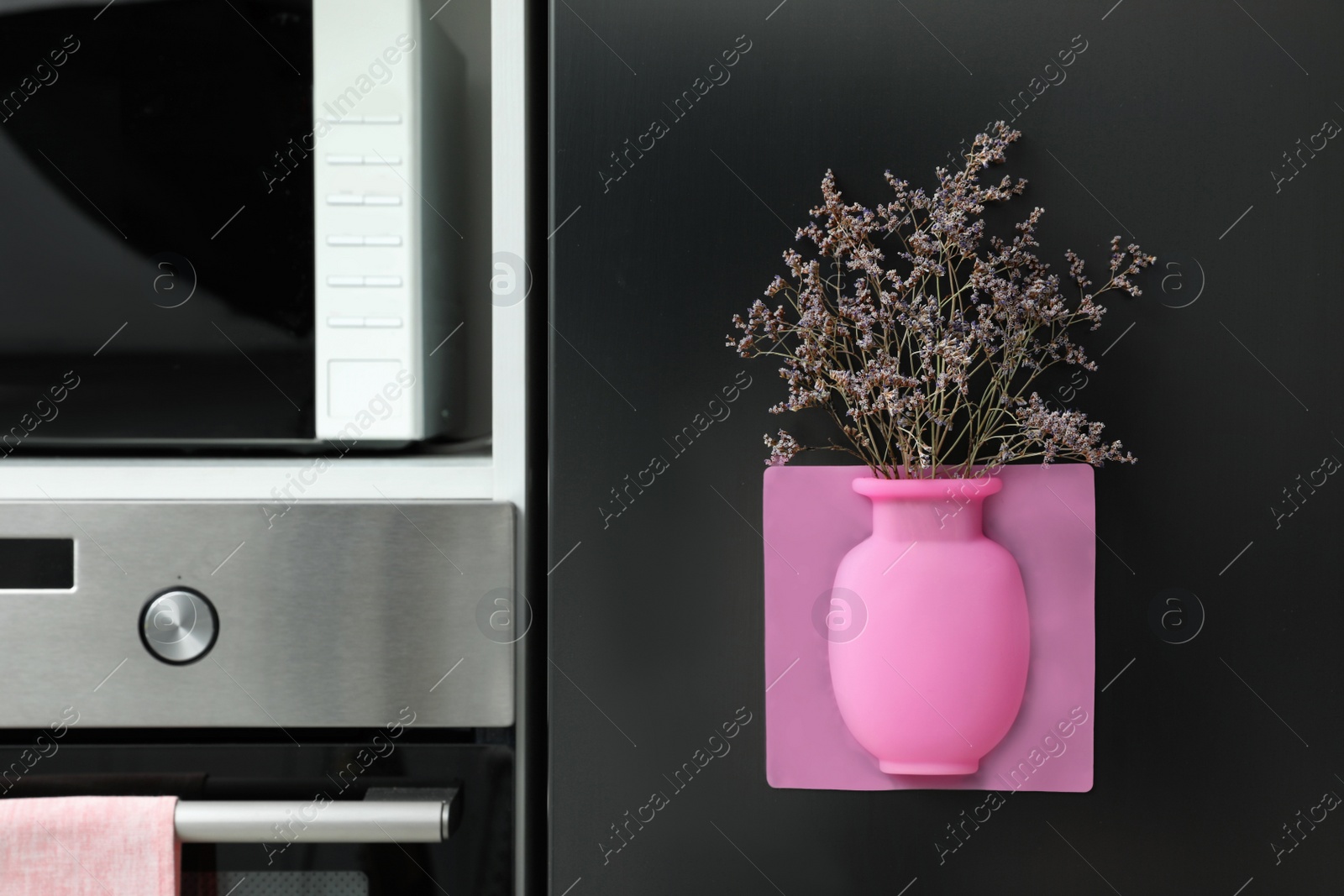 Photo of Silicone vase with beautiful violet flowers on fridge in kitchen, space for text