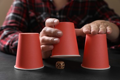Photo of Woman playing thimblerig game with red cups and dice at black table, closeup