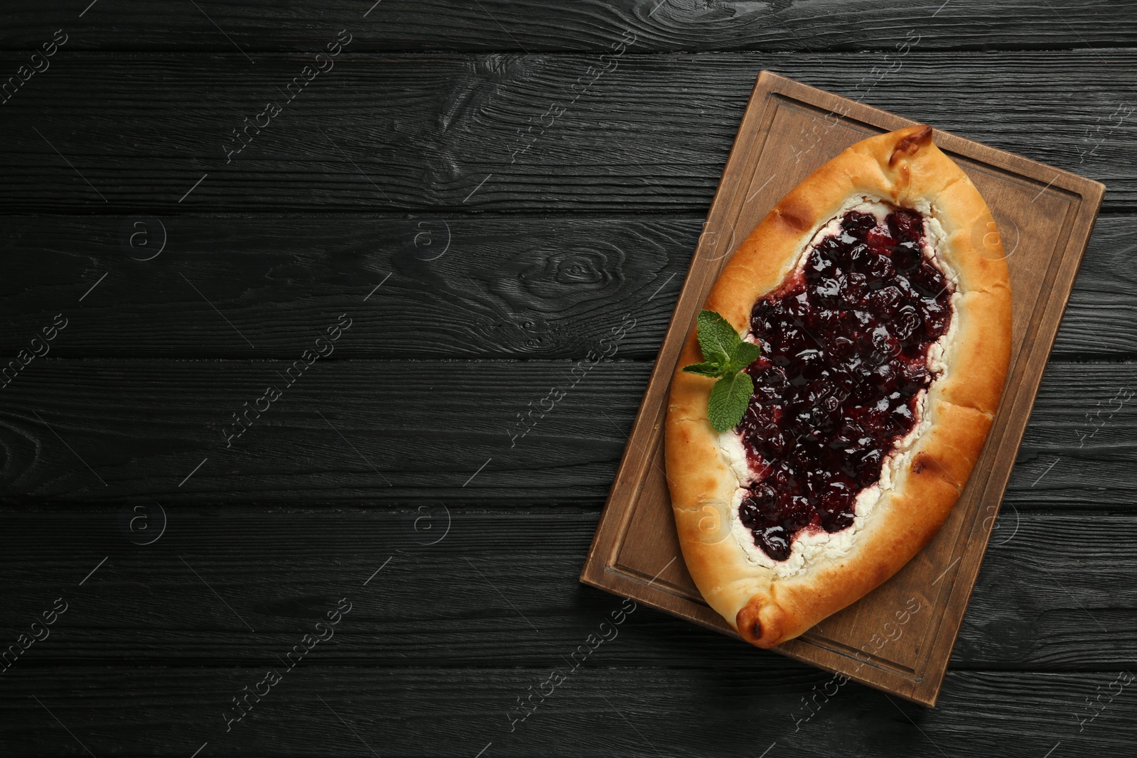 Photo of Delicious sweet cottage cheese pastry with cherry jam on black wooden table, top view. Space for text