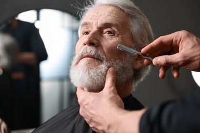 Photo of Professional barber shaving client's beard with blade in barbershop