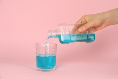Photo of Woman pouring mouthwash into glass on pink background, closeup