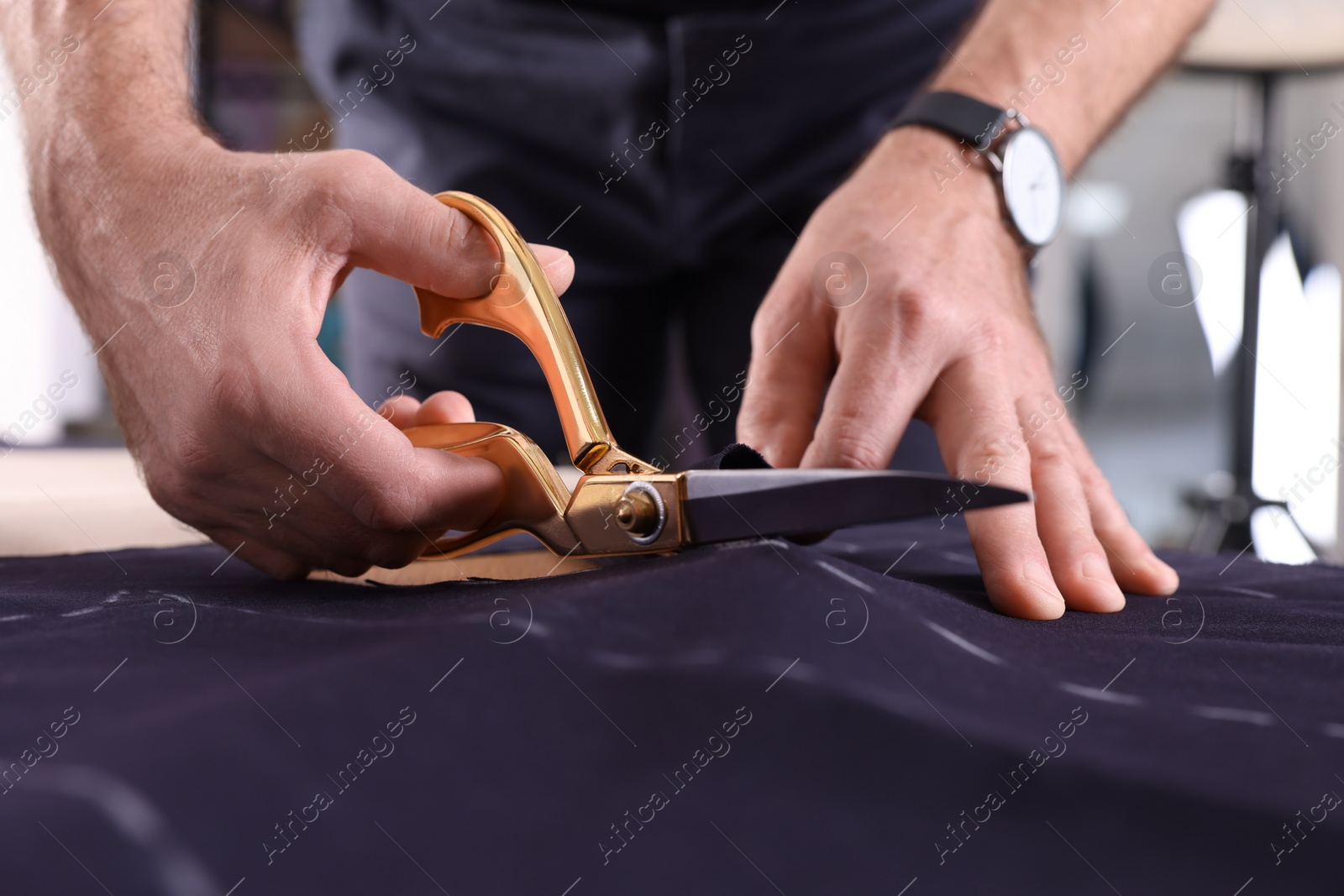 Photo of Professional tailor cutting fabric by following chalked sewing pattern at table, closeup