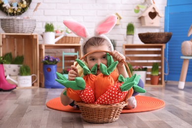 Photo of Adorable little girl with bunny ears and basket full of toy carrots in Easter photo zone