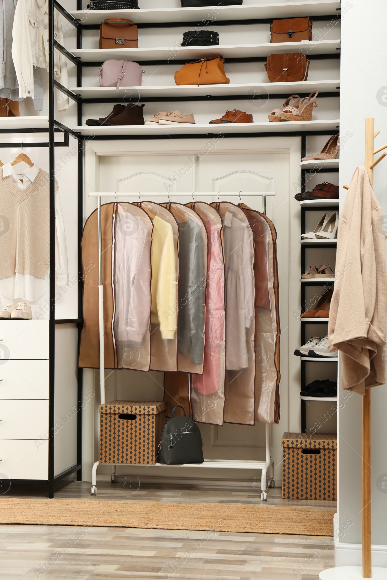 Photo of Garment bags with clothes on rack in dressing room