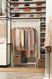 Photo of Garment bags with clothes on rack in dressing room