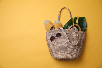 Stylish straw bag and summer accessories on yellow background, flat lay. Space for text