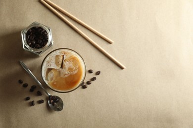 Photo of Refreshing iced coffee with milk in glass, straws and beans on beige background, flat lay. Space for text