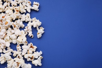 Photo of Tasty popcorn scattered on blue background, space for text