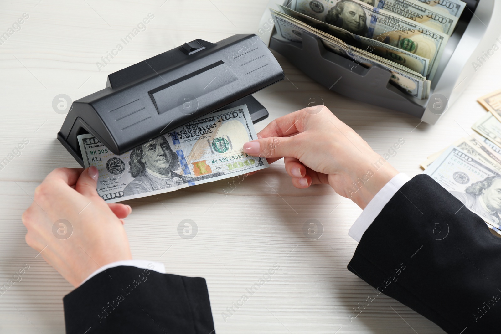 Photo of Woman checking dollar banknote with currency detector at white wooden table, above view. Money examination device