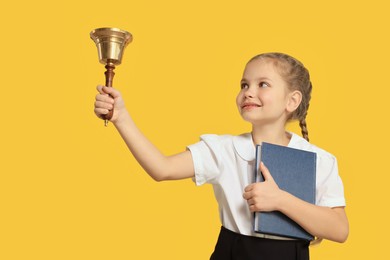 Photo of Pupil with school bell and book on yellow background