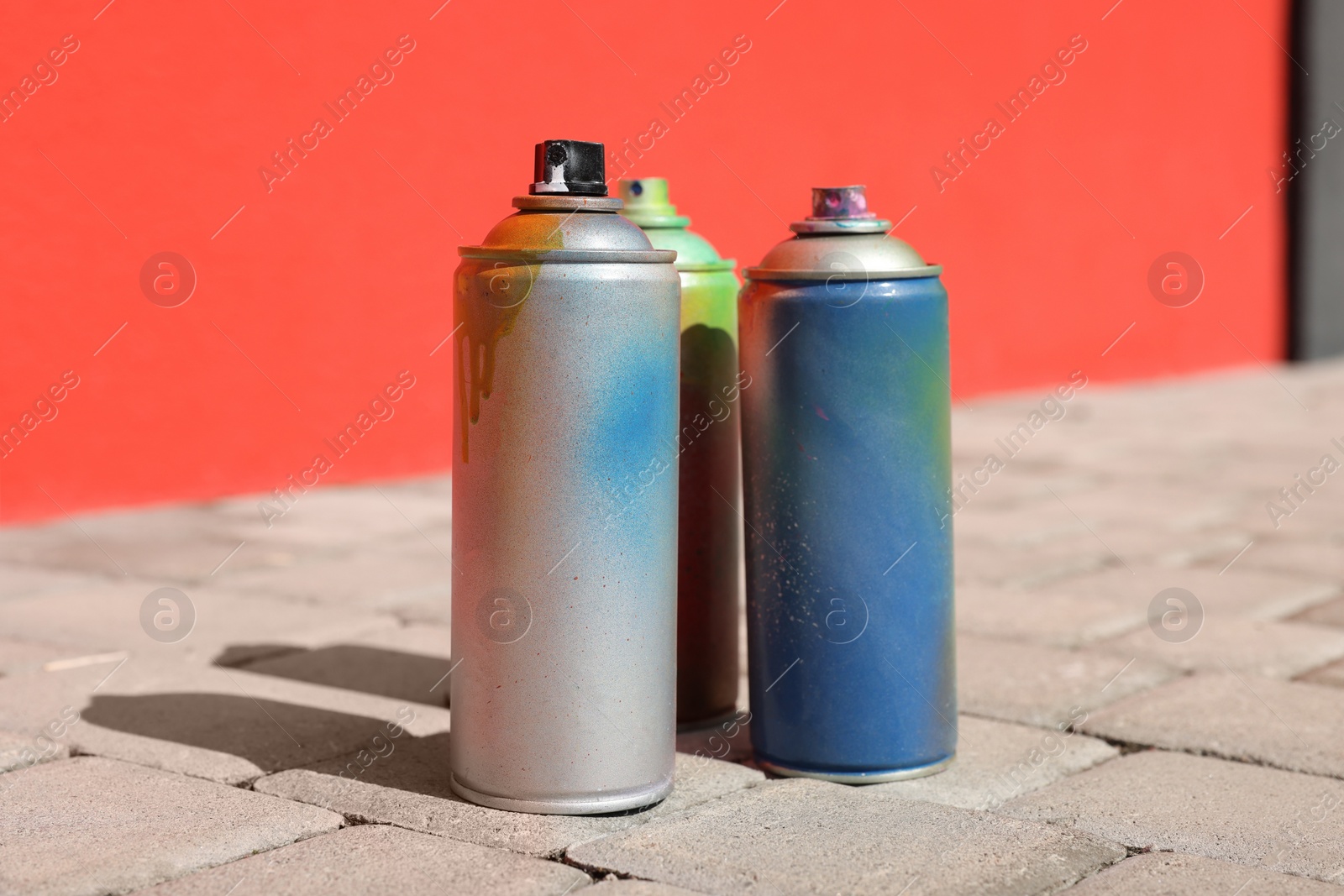 Photo of Cans of different spray paints on pavement near wall, closeup