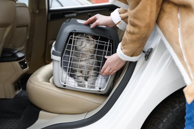 Photo of Woman putting carrier with cute Scottish fold cat into car, closeup