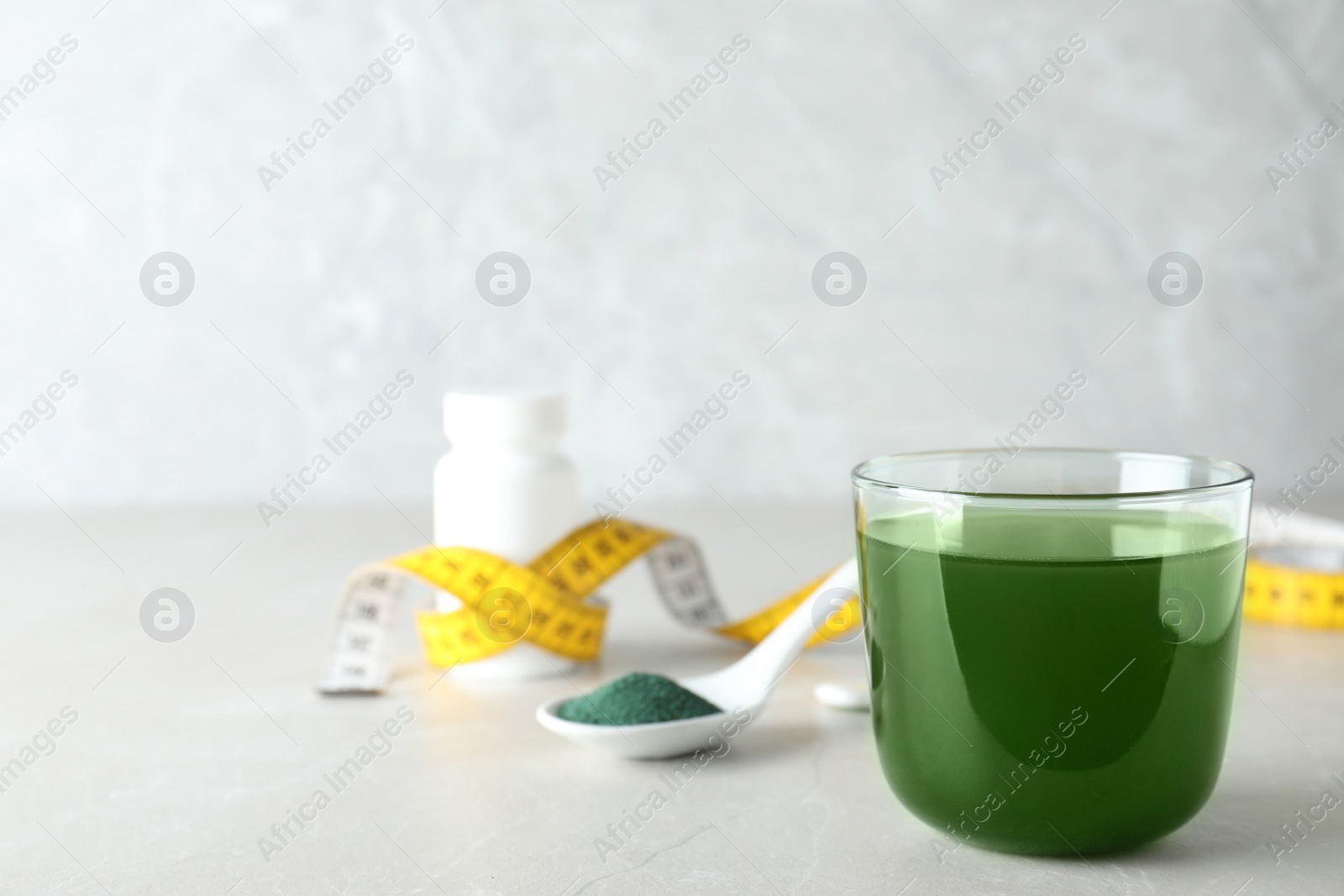 Photo of Glass of spirulina drink and powder on table, space for text