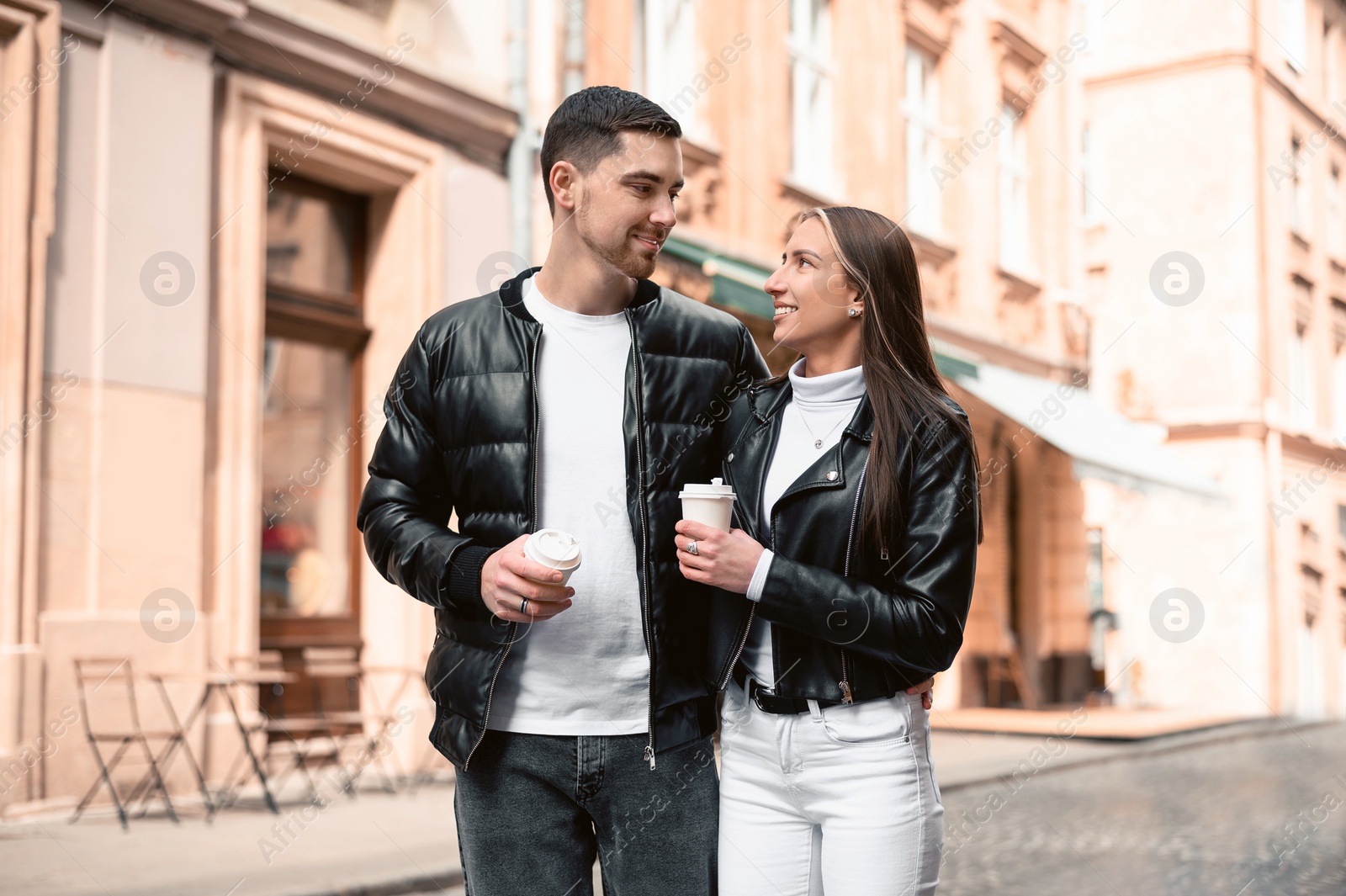 Photo of Lovely young couple with cups of coffee walking together on city street. Romantic date