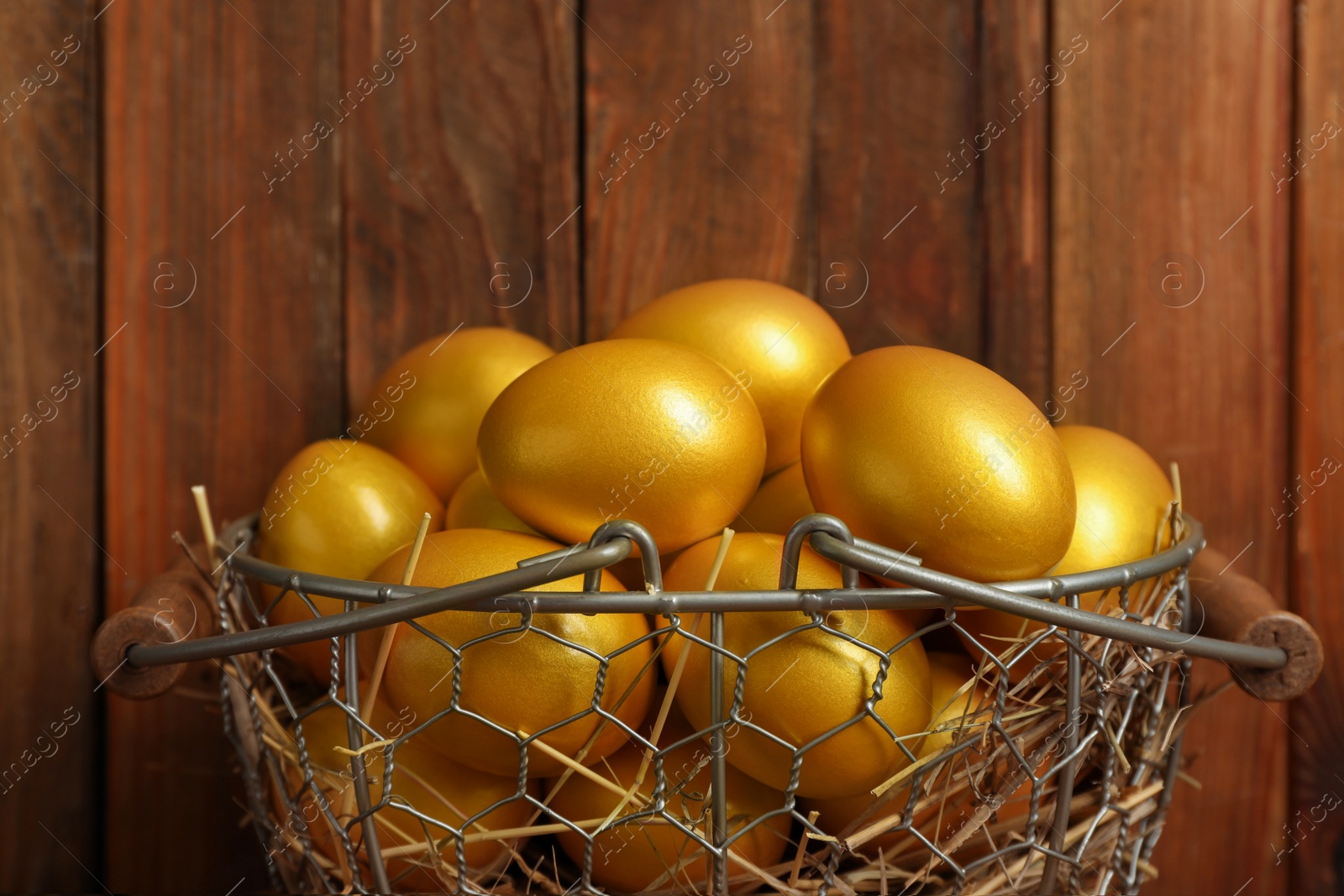 Photo of Shiny golden eggs in metal basket on wooden background
