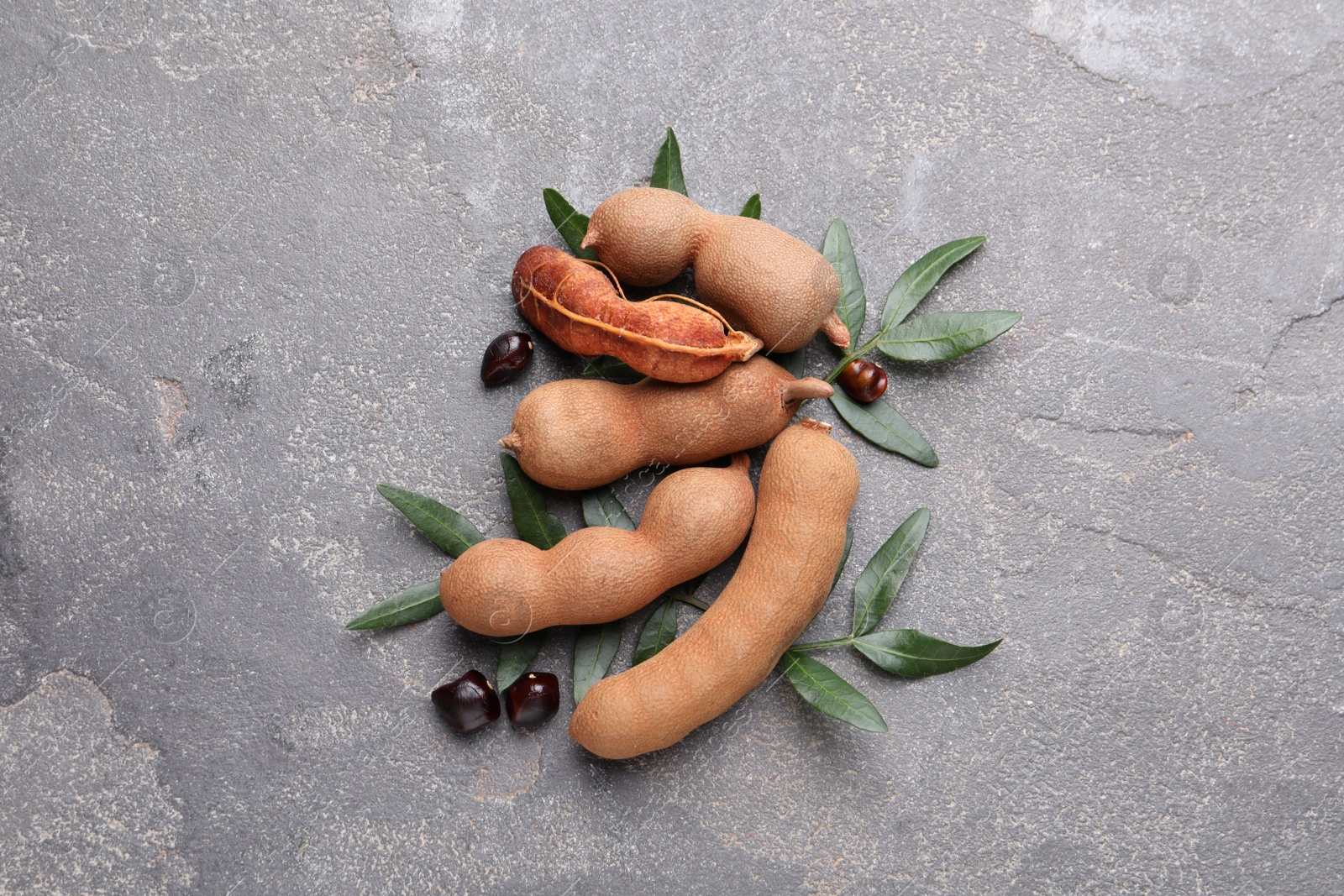 Photo of Ripe tamarinds and fresh leaves on grey table, flat lay