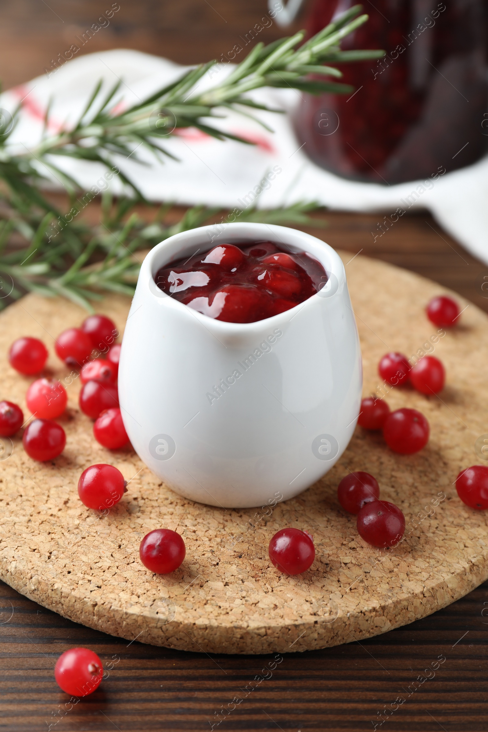 Photo of Cranberry sauce in pitcher and fresh berries on wooden table, closeup