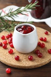 Photo of Cranberry sauce in pitcher and fresh berries on wooden table, closeup