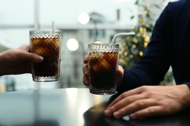 Photo of Couple with glasses of cold cola at table in cafe, closeup