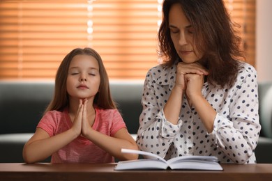 Photo of Mature woman with her little granddaughter praying together over Bible at home