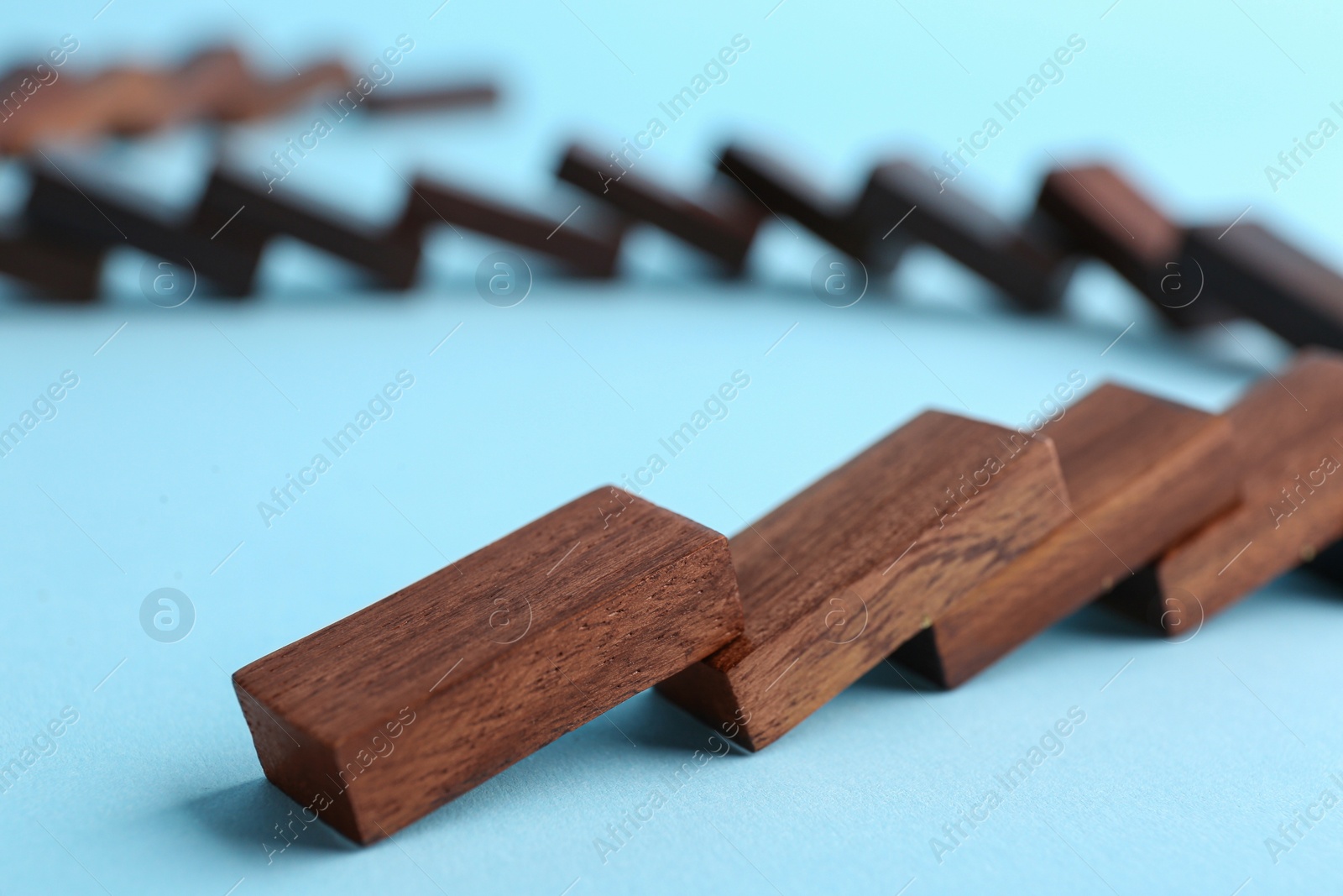 Photo of Falling wooden domino tiles on light blue background, closeup