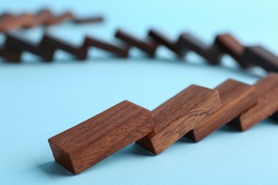 Falling wooden domino tiles on light blue background, closeup