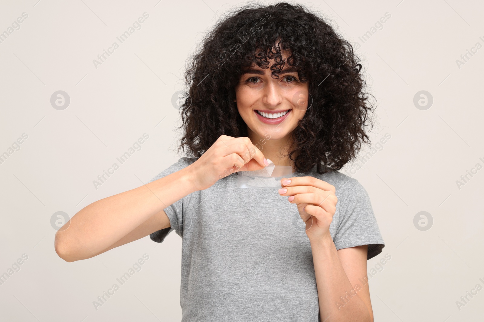 Photo of Young woman holding teeth whitening strips on light grey background