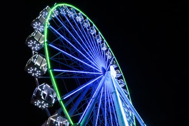 Photo of Beautiful glowing Ferris wheel against dark sky, low angle view