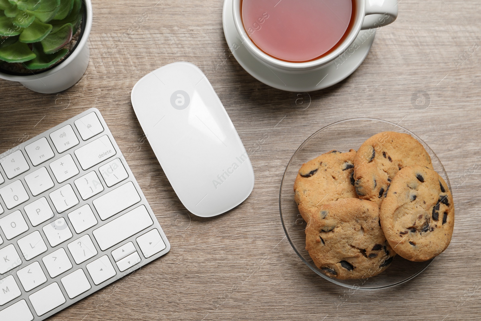 Photo of Chocolate chip cookies, tea and keyboard on wooden table at workplace, flat lay