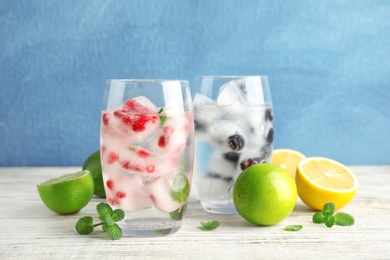 Glasses of drinks with fruit ice cubes on table against color background