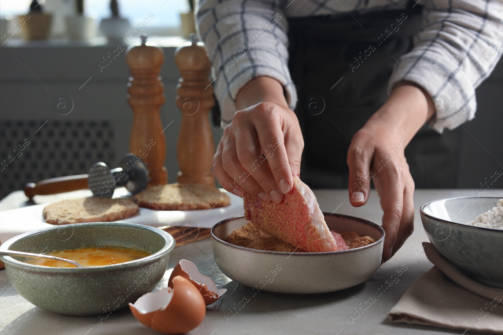 Photo of Woman cooking schnitzel at grey table indoors, closeup