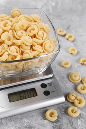 Photo of Kitchen scale with bowl of pasta on grey textured table, closeup