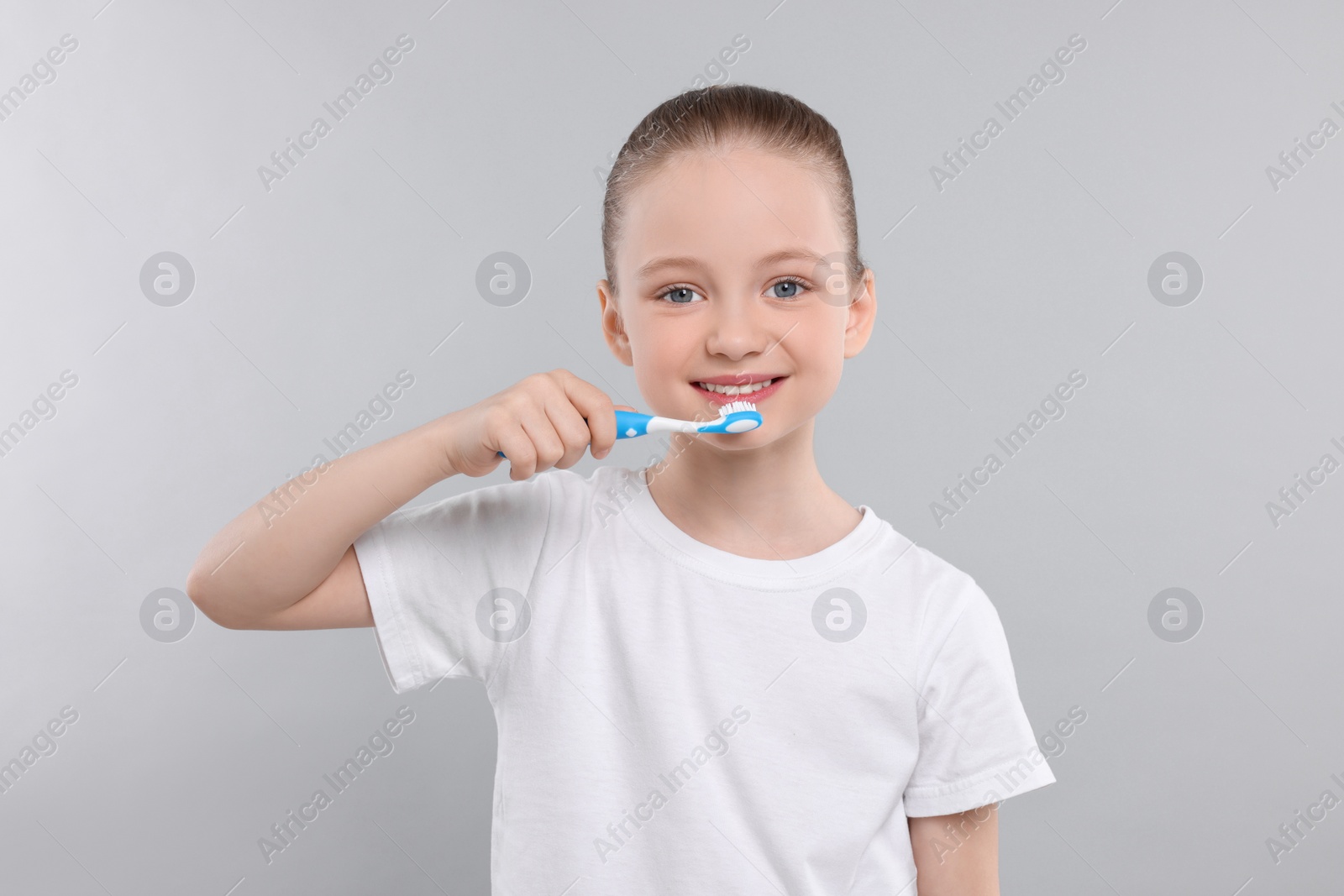 Photo of Happy girl brushing her teeth with toothbrush on light grey background