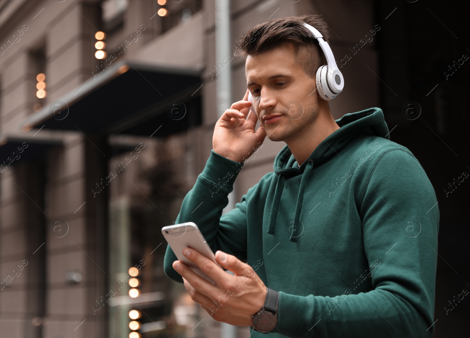 Photo of Portrait of handsome man with headphones and smartphone listening to music on city street. Space for text