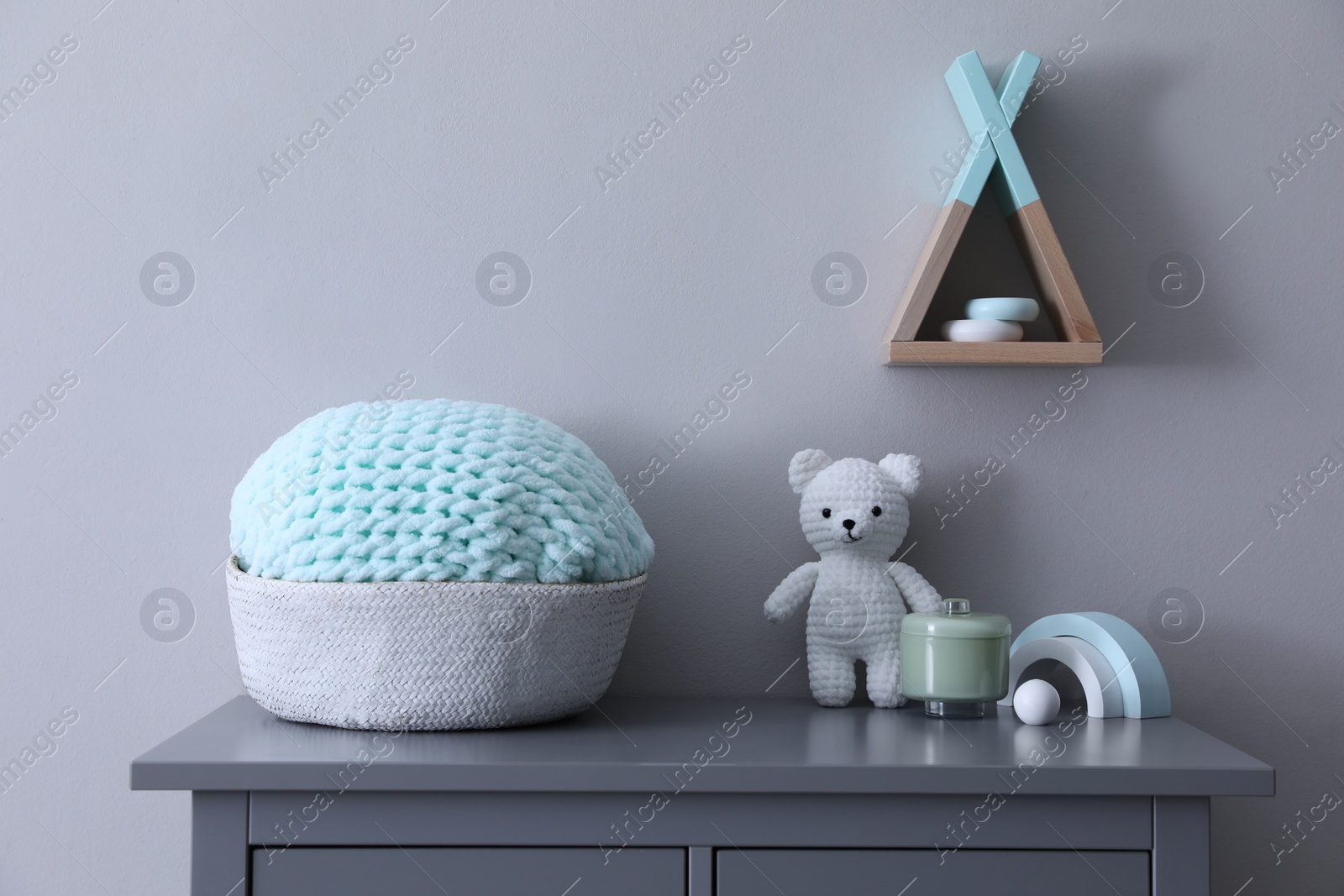 Photo of Child's toys and wicker basket on chest of drawers near light grey wall indoors