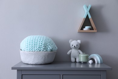 Child's toys and wicker basket on chest of drawers near light grey wall indoors