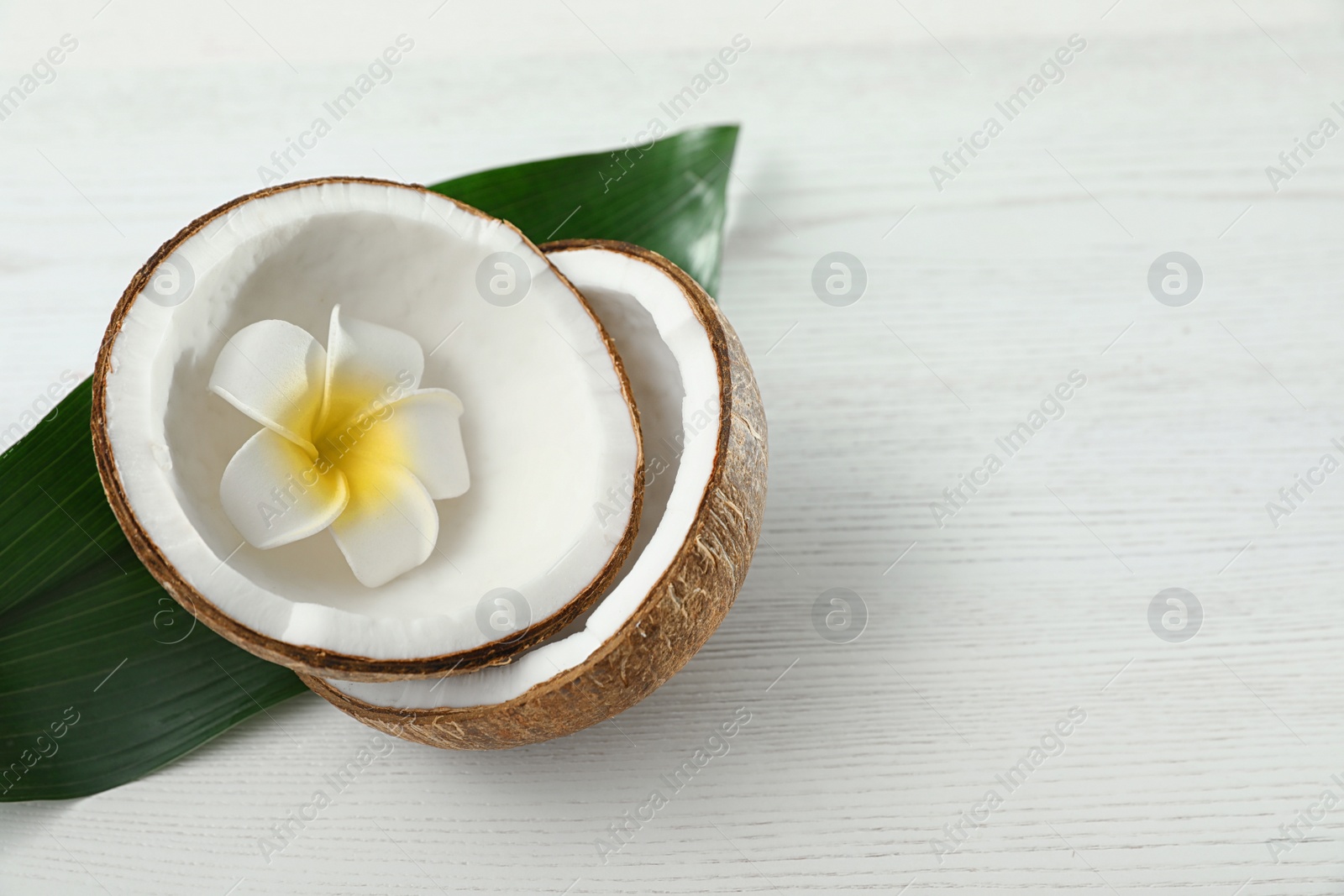 Photo of Composition with halves of coconut on white wooden background. Space for text