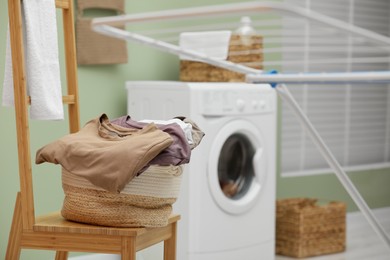 Laundry basket filled with clothes on chair in bathroom. Space for text