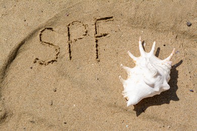 Photo of Abbreviation SPF written on sand and seashell at beach, top view