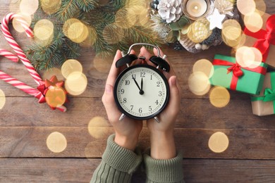 Photo of Woman holding alarm clock near Christmas decor over wooden background, top view. New Year countdown