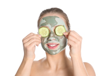 Beautiful woman with clay mask on her face holding cucumber slices against white background