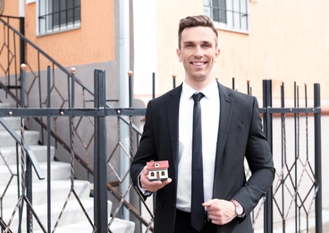 Photo of Male real estate agent with house model outdoors