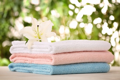 Pile of fresh towels and flower on table against blurred background, space for text