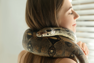 Photo of Young woman with boa constrictor at home, closeup. Exotic pet