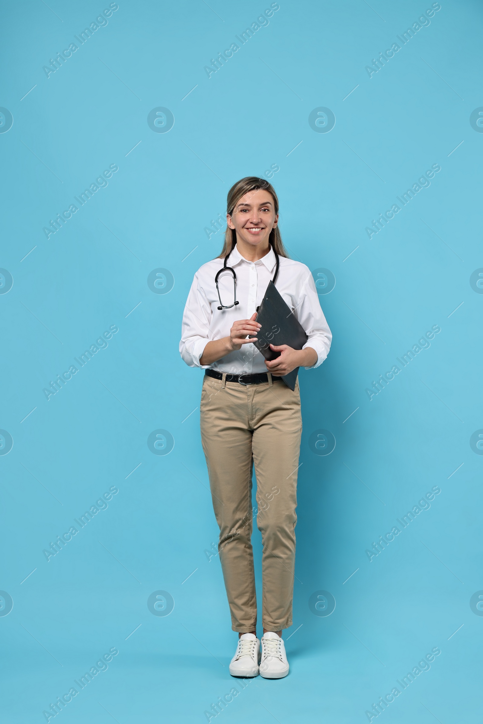 Photo of Portrait of happy doctor with stethoscope and clipboard on light blue background