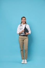 Photo of Portrait of happy doctor with stethoscope and clipboard on light blue background