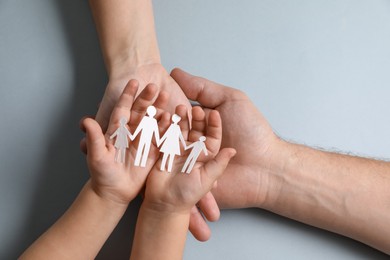 Photo of Parents and child holding paper family figures on gray background, top view